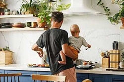 ein Vater trägt sein Baby auf dem Arm und kocht