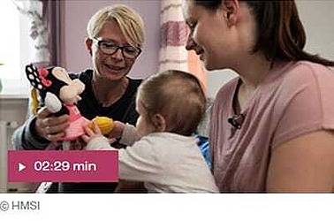 Bildausschnitt aus Video: Baby sitzt auf Schoß von Mutter und greift nach einer Minimaus