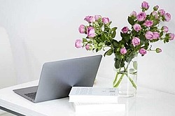weißer Schreibtisch mit Laptop und rosa Blumen