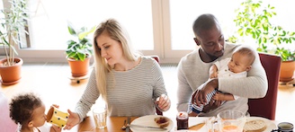 Eine Familie mit zwei kleinen Kindern sitzt um einen Esstisch und frühstückt.