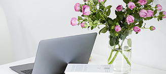 weißer Schreibtisch mit Laptop und rosa Blumen